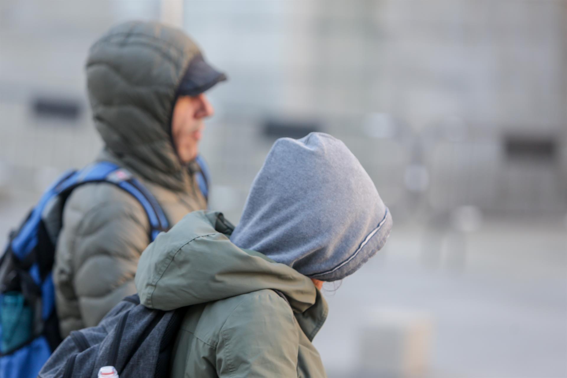 Dos jovenes se protegen del frío con abrigos y gorros mientras pasean durante un día de viento por Madrid / Europa Press