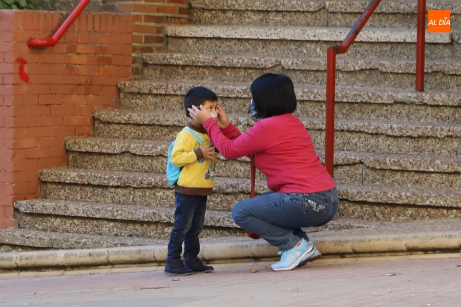 Una mujer coloca la mascarilla a su hijo a la entrada al colegio